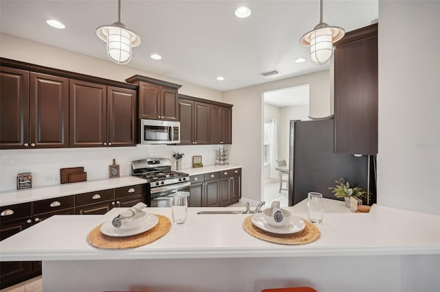 kitchen with appliances with stainless steel finishes, backsplash, dark brown cabinets, and pendant lighting