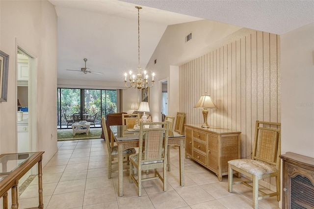 dining space with lofted ceiling, light tile patterned floors, ceiling fan with notable chandelier, and wooden walls