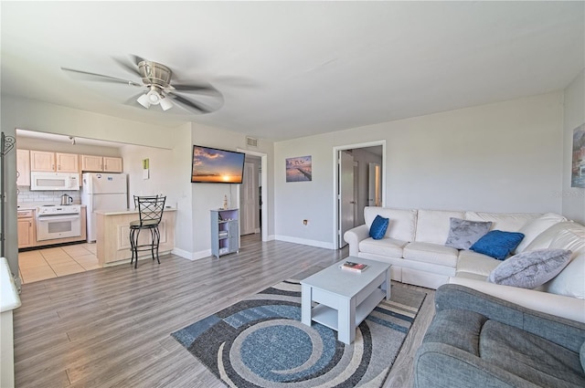 living room featuring light wood finished floors, visible vents, baseboards, and a ceiling fan