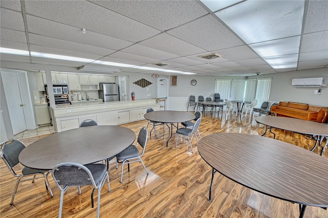 dining room featuring a drop ceiling, light wood-style flooring, a wall mounted air conditioner, and visible vents