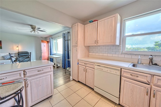 kitchen with light countertops, light brown cabinets, white dishwasher, and a sink