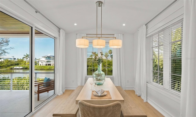 dining room featuring a notable chandelier, a water view, vaulted ceiling, and light wood-type flooring