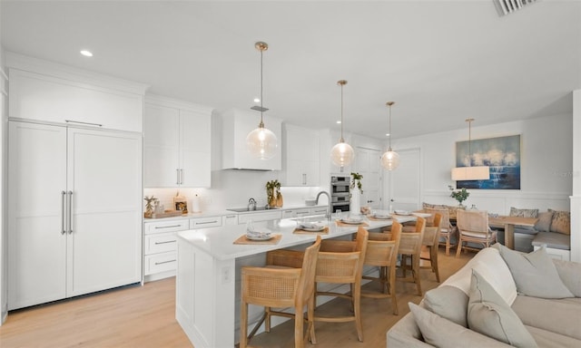 kitchen with a kitchen bar, light wood-type flooring, black cooktop, a center island with sink, and white cabinets