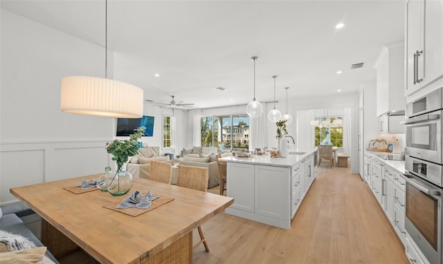 kitchen featuring white cabinets, ceiling fan, light hardwood / wood-style floors, and an island with sink