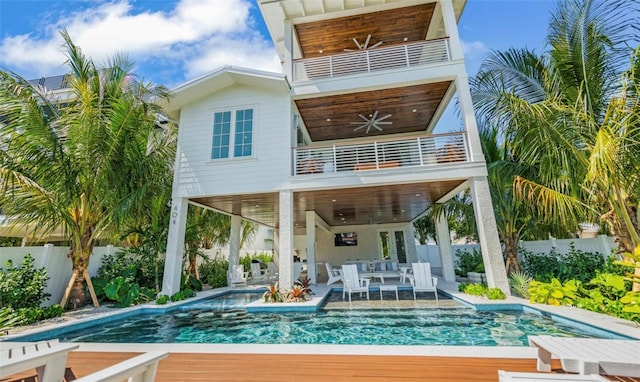 rear view of house with ceiling fan, a balcony, and a fenced in pool