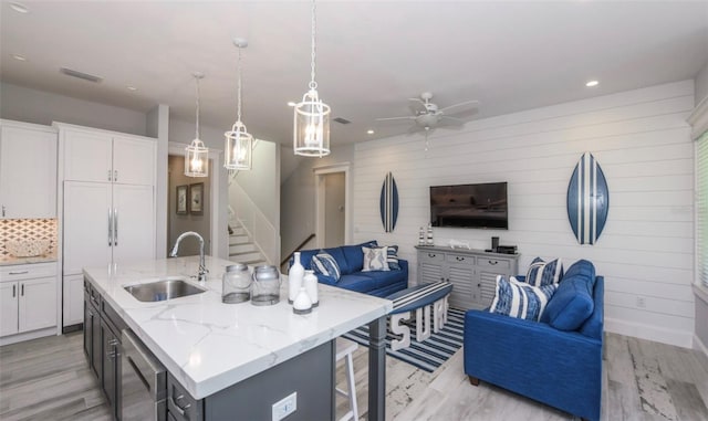 kitchen featuring pendant lighting, a center island with sink, sink, light wood-type flooring, and white cabinetry