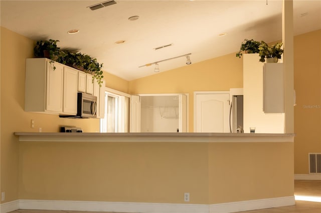 kitchen featuring rail lighting, kitchen peninsula, lofted ceiling, white cabinets, and appliances with stainless steel finishes