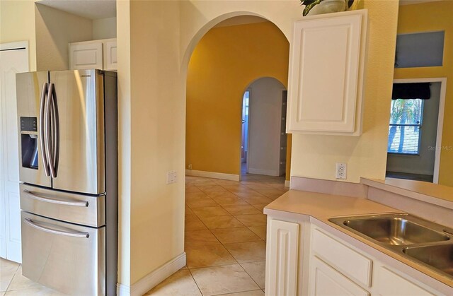 kitchen with white cabinets, stainless steel fridge, light tile patterned floors, and sink