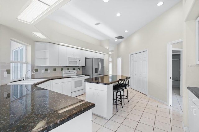 kitchen with tasteful backsplash, white appliances, sink, white cabinets, and a kitchen island