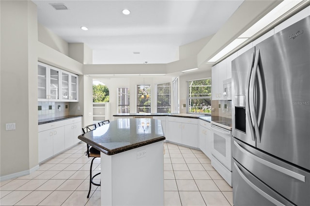 kitchen with tasteful backsplash, white appliances, a kitchen island, white cabinetry, and a breakfast bar area