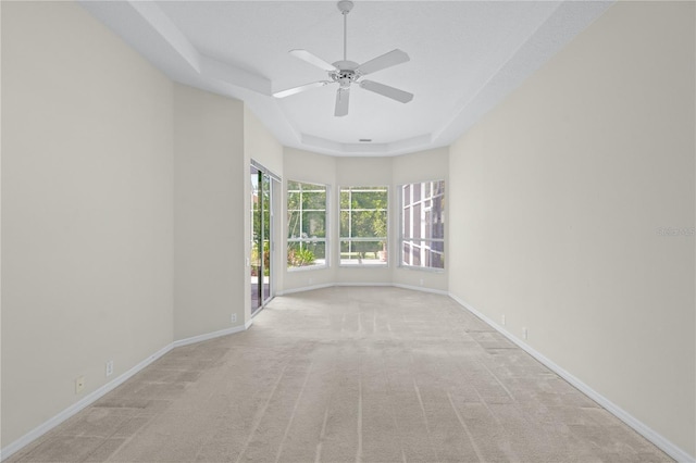 empty room featuring light carpet, a raised ceiling, and ceiling fan