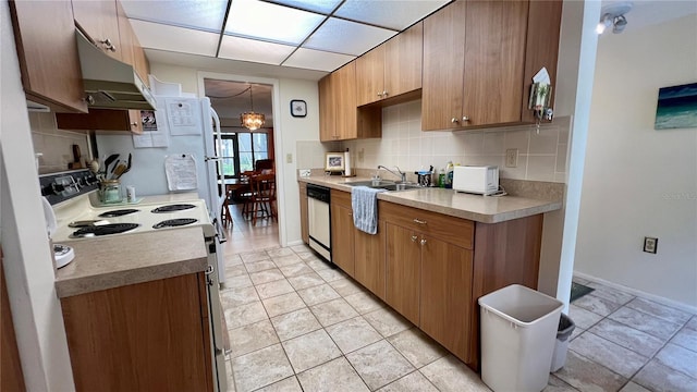 kitchen with white appliances, backsplash, light countertops, under cabinet range hood, and a sink