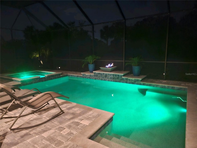 pool at night featuring a lanai, a patio area, and an in ground hot tub