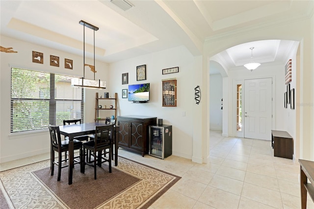 dining room with a tray ceiling, light tile patterned flooring, beverage cooler, and ornamental molding