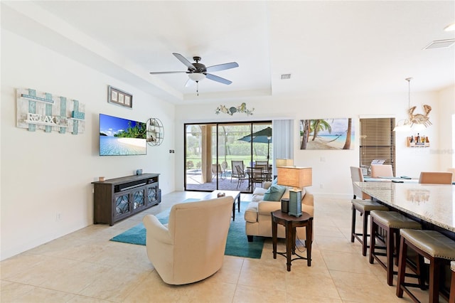 tiled living room with a raised ceiling and ceiling fan with notable chandelier