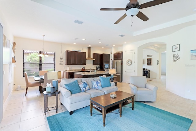 living room featuring sink, light tile patterned flooring, and ceiling fan with notable chandelier