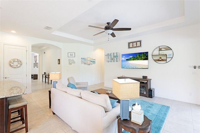 living room with light tile patterned floors, a raised ceiling, and ceiling fan