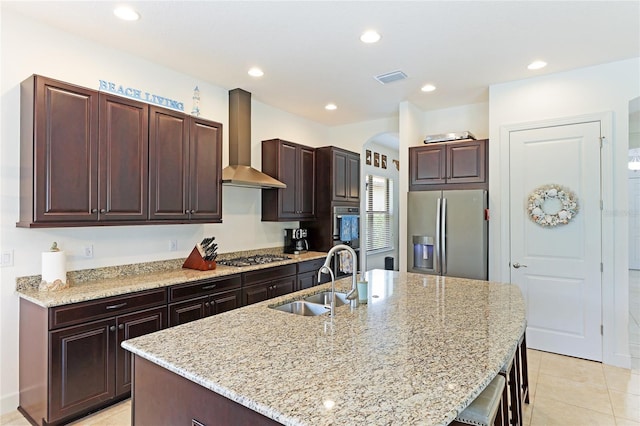 kitchen with sink, wall chimney exhaust hood, a breakfast bar area, a kitchen island with sink, and appliances with stainless steel finishes