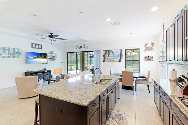 kitchen featuring ceiling fan, sink, hanging light fixtures, a tray ceiling, and a kitchen island with sink