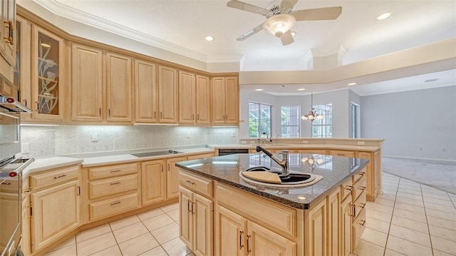 kitchen with a center island with sink, ceiling fan with notable chandelier, dark stone counters, light carpet, and light brown cabinets