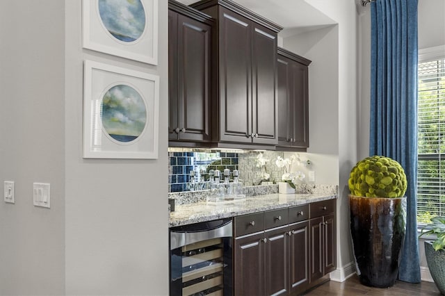 bar featuring decorative backsplash, dark brown cabinets, wine cooler, and light stone countertops