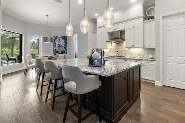 kitchen featuring pendant lighting, wall chimney range hood, a large island, white cabinetry, and a breakfast bar area