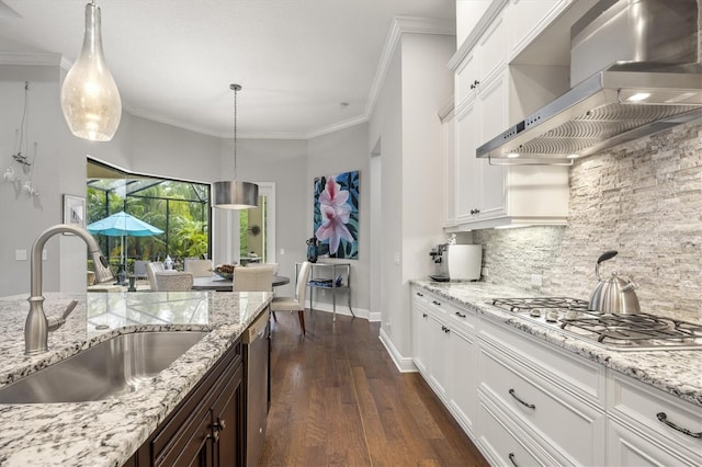 kitchen with ornamental molding, sink, wall chimney range hood, decorative light fixtures, and white cabinetry