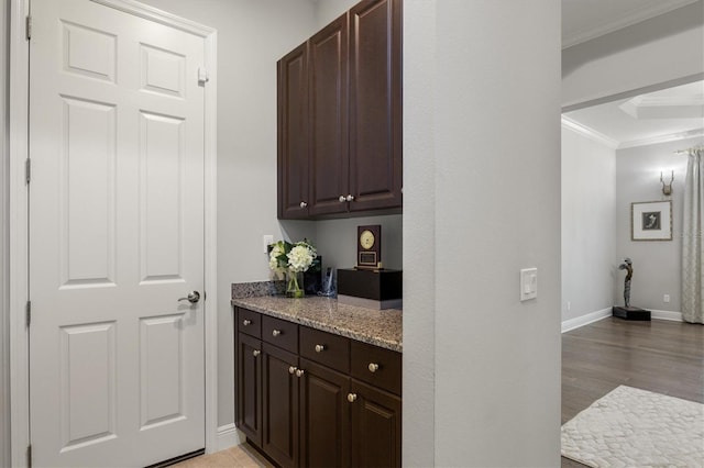 bar with dark brown cabinetry, light stone countertops, light hardwood / wood-style floors, and ornamental molding