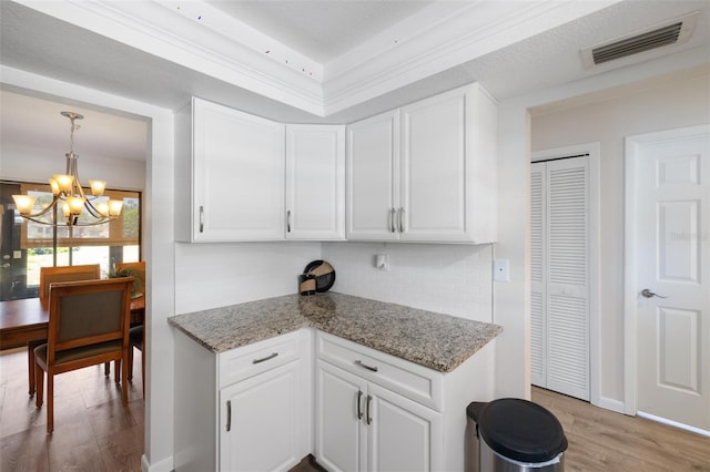 kitchen with an inviting chandelier, white cabinets, decorative light fixtures, light hardwood / wood-style floors, and light stone counters