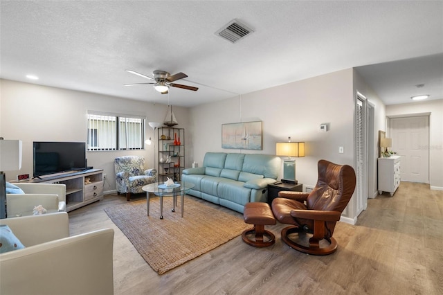 living room with a textured ceiling, light hardwood / wood-style flooring, and ceiling fan