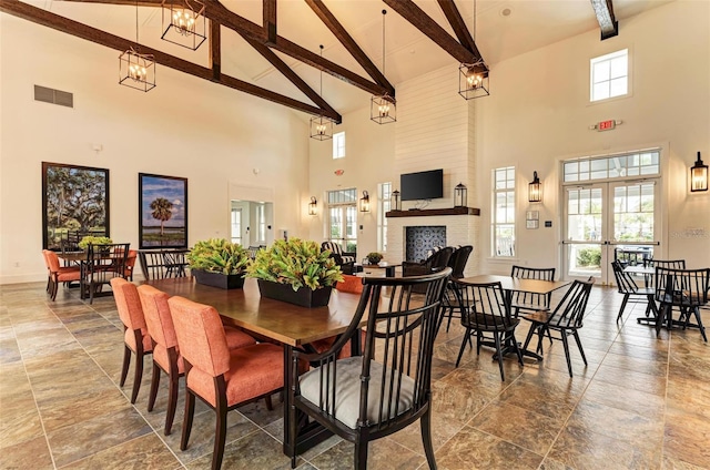 dining room with french doors, an inviting chandelier, beamed ceiling, a towering ceiling, and a fireplace