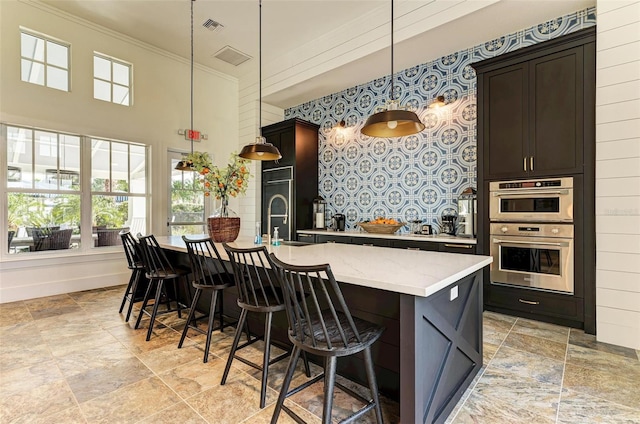 kitchen with hanging light fixtures, light stone countertops, a kitchen island with sink, and sink