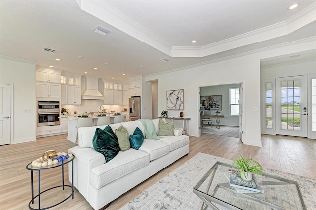 living room with crown molding, a raised ceiling, and light hardwood / wood-style flooring