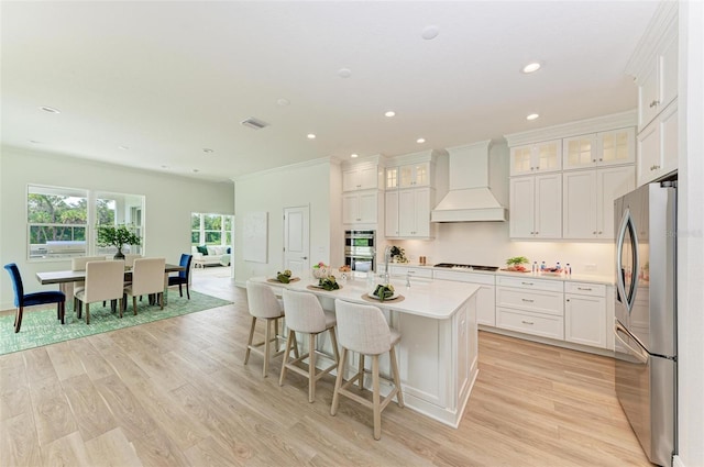 kitchen featuring stainless steel appliances, premium range hood, a center island with sink, and white cabinetry