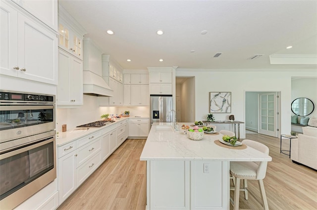 kitchen featuring a kitchen island with sink, stainless steel appliances, light stone counters, white cabinets, and custom exhaust hood