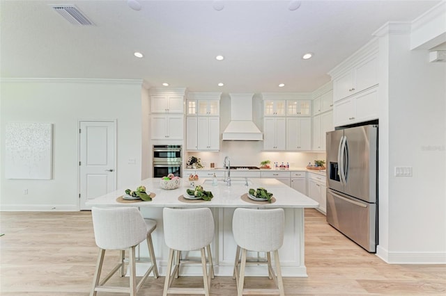 kitchen featuring a kitchen island with sink, stainless steel appliances, white cabinets, and premium range hood