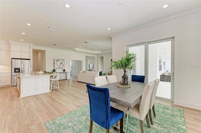 dining room featuring crown molding, a raised ceiling, and light hardwood / wood-style floors