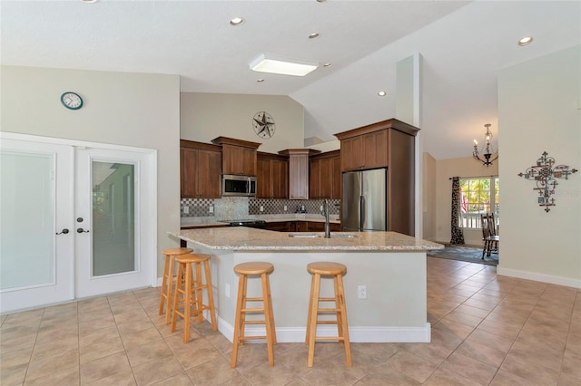 kitchen with sink, stainless steel appliances, an island with sink, and light stone counters