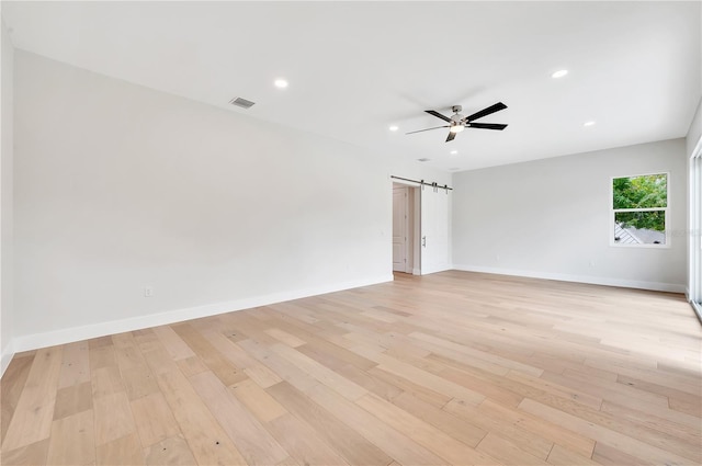 empty room with light hardwood / wood-style floors, a barn door, and ceiling fan