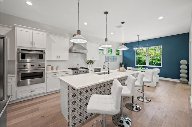 kitchen with sink, wall chimney exhaust hood, hanging light fixtures, and white cabinets