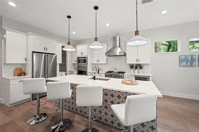 kitchen with pendant lighting, white cabinetry, sink, high end refrigerator, and wall chimney range hood