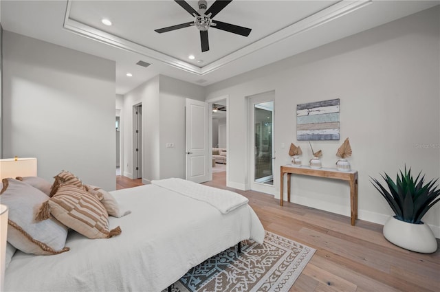 bedroom featuring light hardwood / wood-style floors, ensuite bath, ceiling fan, and a tray ceiling