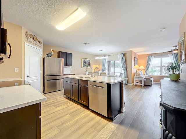 kitchen featuring appliances with stainless steel finishes, dark brown cabinetry, an island with sink, and sink