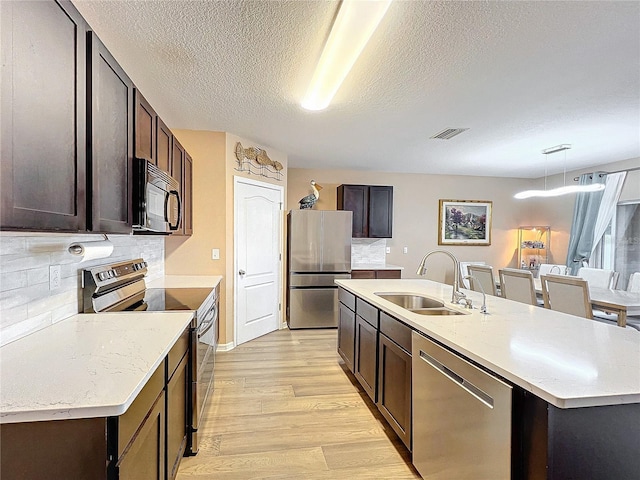 kitchen with sink, stainless steel appliances, tasteful backsplash, decorative light fixtures, and a kitchen island with sink