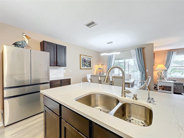 kitchen featuring stainless steel fridge, light stone counters, dark brown cabinetry, sink, and decorative light fixtures