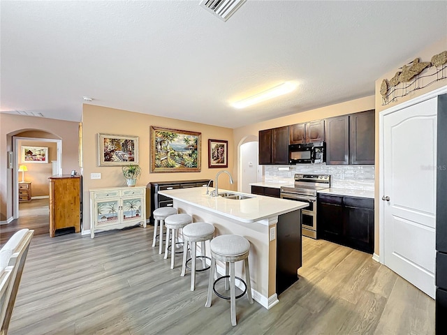 kitchen featuring stainless steel range with electric stovetop, dark brown cabinetry, sink, a breakfast bar area, and an island with sink