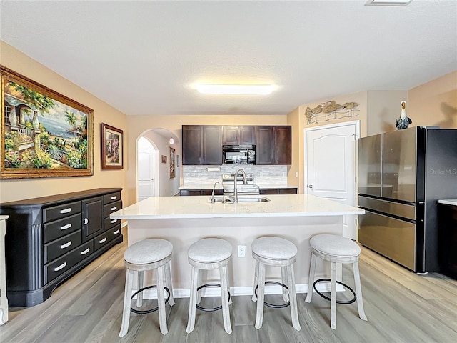 kitchen with sink, stainless steel fridge, backsplash, and an island with sink