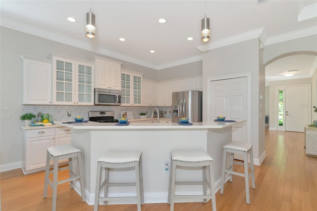 kitchen featuring light wood-type flooring, ornamental molding, stainless steel appliances, pendant lighting, and an island with sink