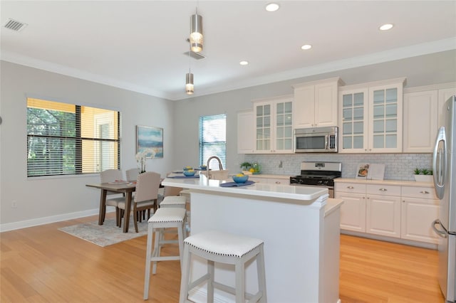 kitchen featuring white cabinets, decorative light fixtures, light wood-type flooring, and appliances with stainless steel finishes