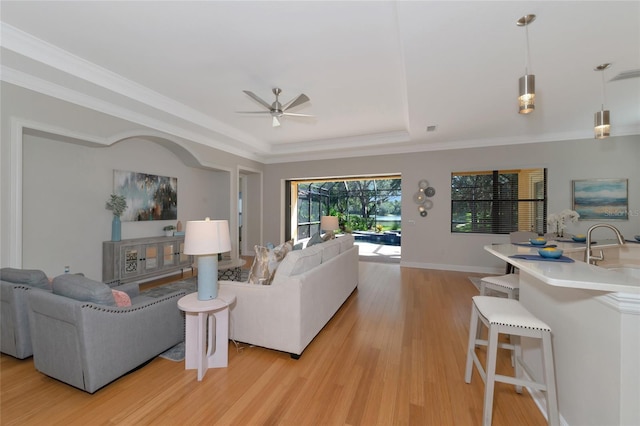 living room featuring a raised ceiling, sink, ceiling fan, ornamental molding, and light hardwood / wood-style floors